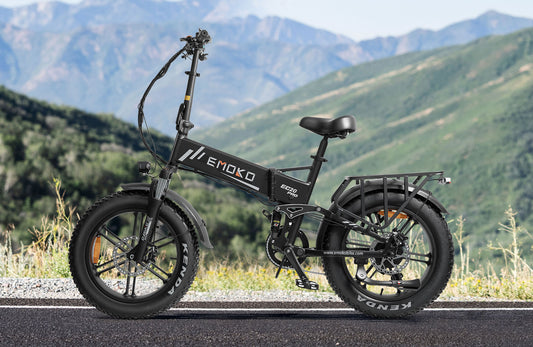 Black EMOKO EC20 Pro electric bike with fat Kenda tires on road with mountain background